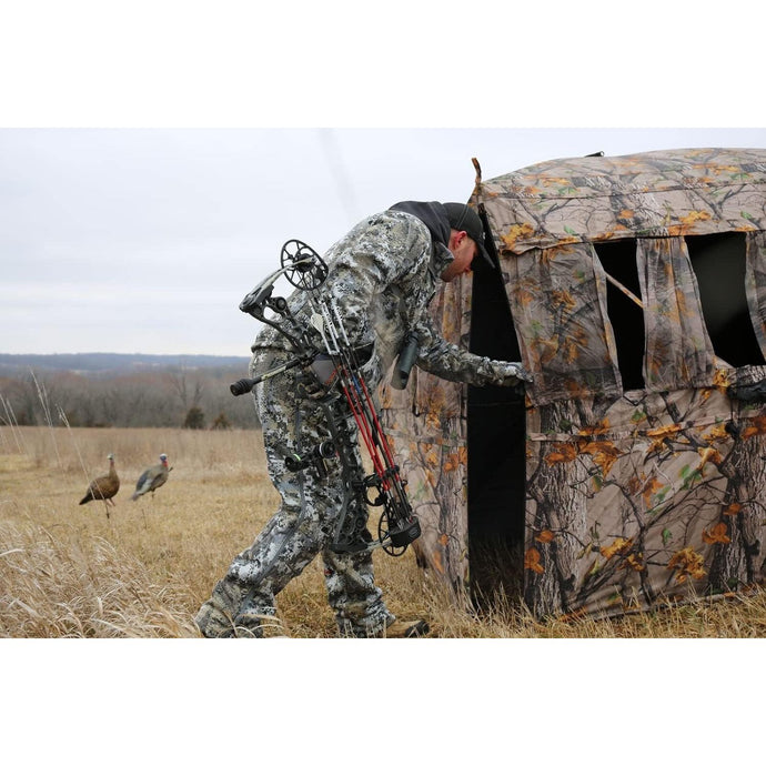 An outdoor scene featuring a muddy terrain with a Tente VS360 tent set up, showcasing its spacious design and vibrant colors against a backdrop of nature.